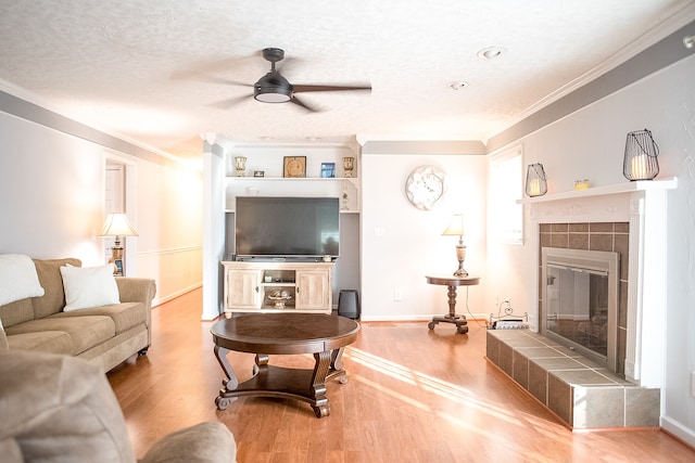 living room with ornamental molding, a textured ceiling, ceiling fan, a tile fireplace, and hardwood / wood-style flooring