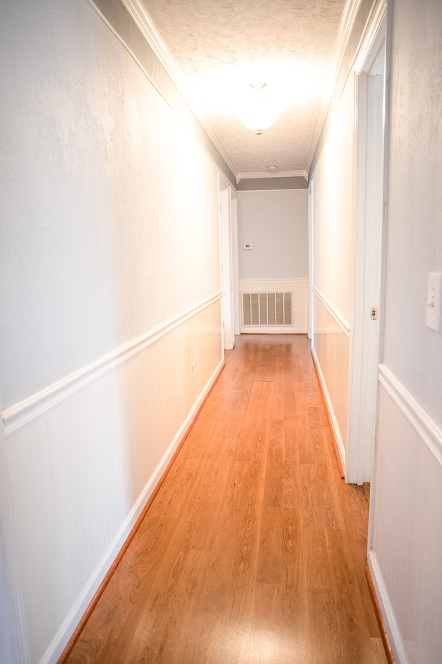 hallway with a textured ceiling, light wood-type flooring, and crown molding