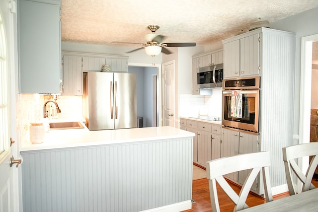 kitchen featuring ceiling fan, sink, stainless steel appliances, light hardwood / wood-style flooring, and decorative backsplash