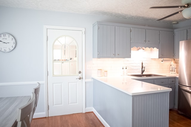 kitchen featuring kitchen peninsula, a textured ceiling, sink, wood-type flooring, and stainless steel refrigerator