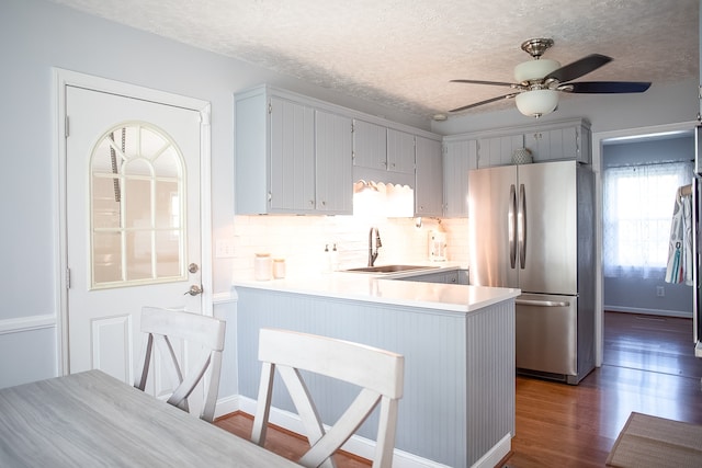 kitchen featuring kitchen peninsula, stainless steel fridge, dark hardwood / wood-style flooring, ceiling fan, and sink