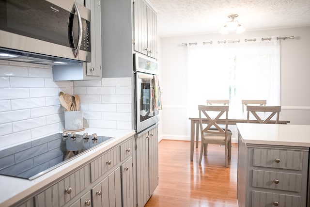 kitchen with gray cabinets, a healthy amount of sunlight, light hardwood / wood-style flooring, and stainless steel appliances