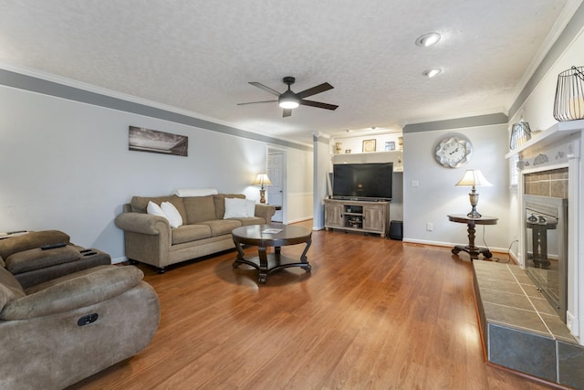 living room with a tile fireplace, hardwood / wood-style flooring, ceiling fan, crown molding, and a textured ceiling