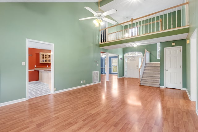 unfurnished living room with high vaulted ceiling, ceiling fan, and light wood-type flooring