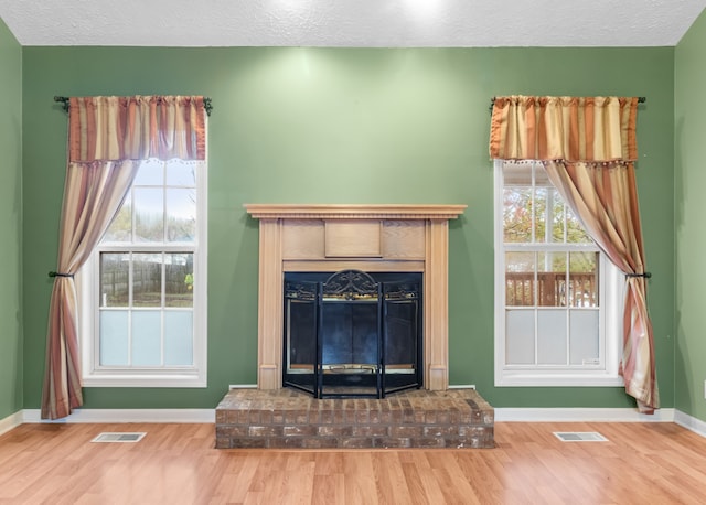 unfurnished living room featuring a brick fireplace, a textured ceiling, wood-type flooring, and a healthy amount of sunlight