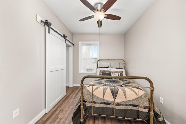 bedroom with ceiling fan, a barn door, and dark hardwood / wood-style floors