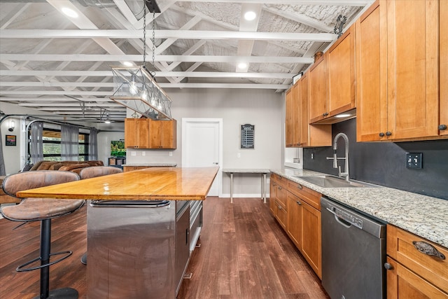 kitchen featuring dark wood-type flooring, dishwasher, sink, light stone countertops, and pendant lighting