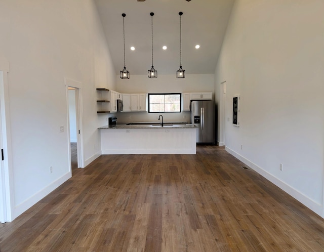 kitchen featuring kitchen peninsula, stainless steel fridge, decorative light fixtures, high vaulted ceiling, and white cabinetry