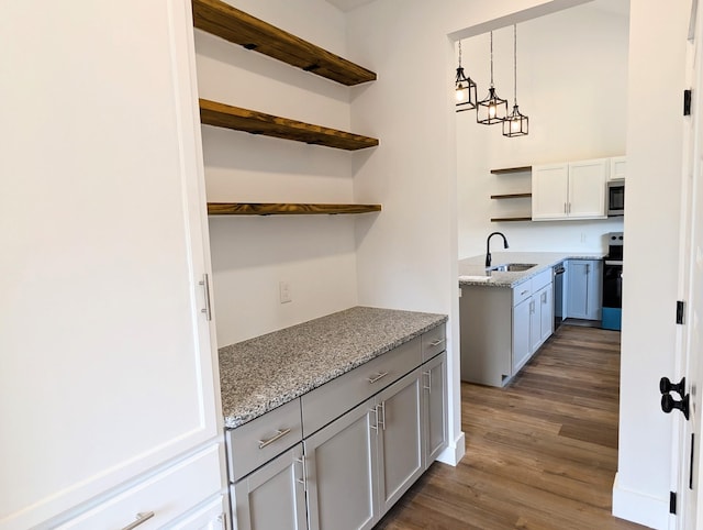 kitchen featuring stainless steel appliances, light stone counters, sink, and hanging light fixtures