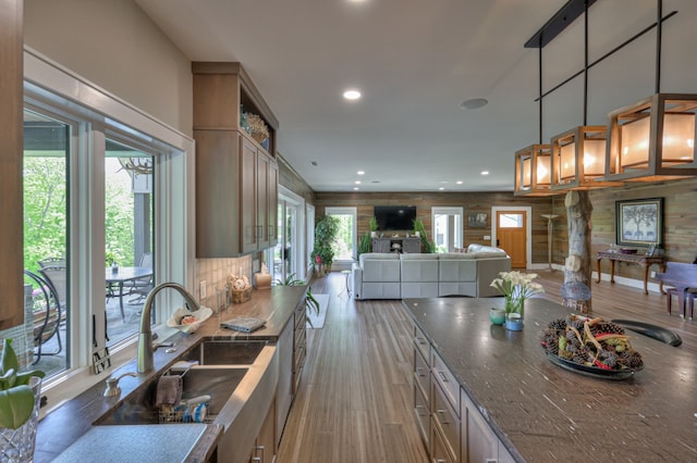 kitchen featuring light wood-type flooring, hanging light fixtures, dark stone counters, and sink