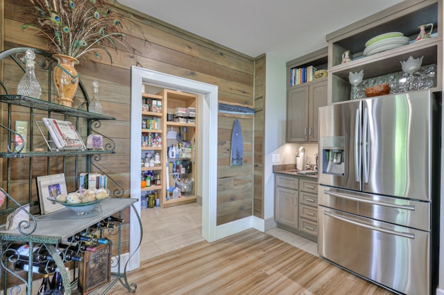 kitchen with light hardwood / wood-style flooring, wood walls, stainless steel fridge with ice dispenser, and gray cabinetry