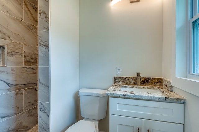 bathroom featuring toilet, vanity, and a tile shower