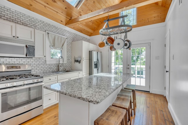 kitchen featuring stainless steel appliances, sink, a kitchen island, vaulted ceiling with skylight, and white cabinetry