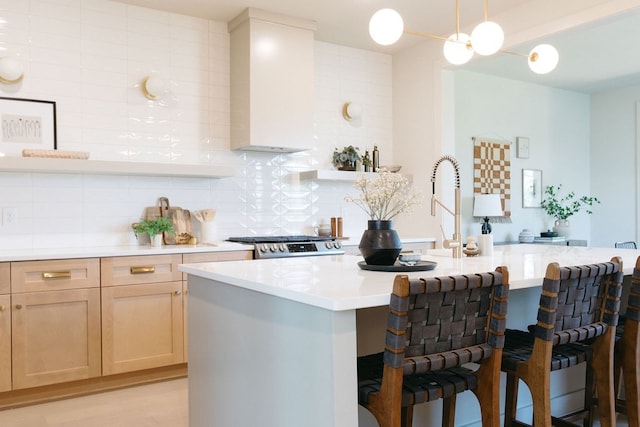 kitchen with light countertops, hanging light fixtures, wall chimney range hood, backsplash, and a center island with sink