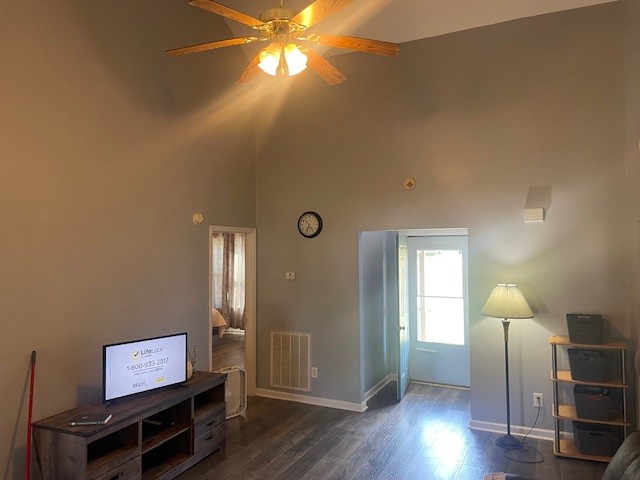 living room featuring a towering ceiling, dark hardwood / wood-style floors, and ceiling fan