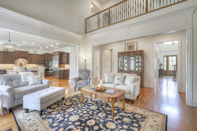 living room with crown molding, a towering ceiling, a chandelier, and light wood-type flooring