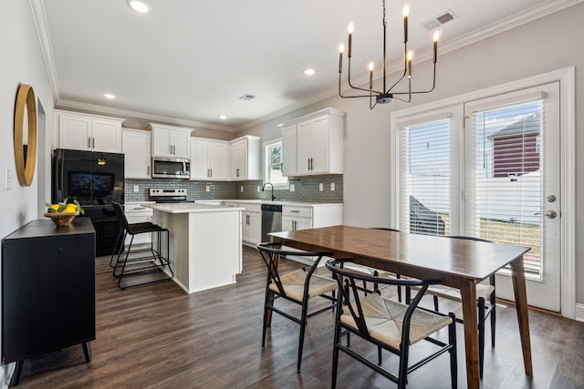 dining area featuring dark wood-type flooring, sink, a notable chandelier, and crown molding