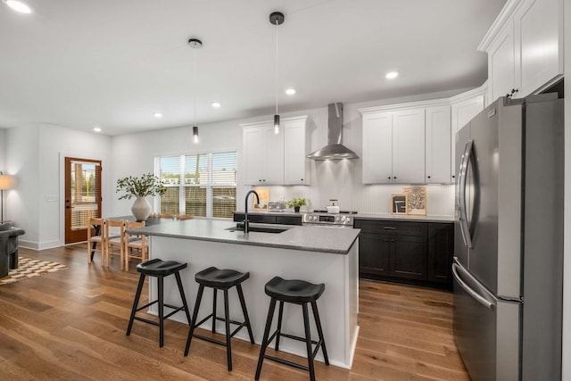 kitchen featuring pendant lighting, sink, wall chimney exhaust hood, an island with sink, and appliances with stainless steel finishes