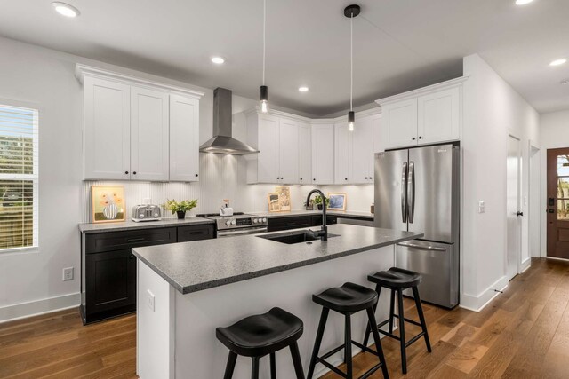 kitchen with wall chimney exhaust hood, dark hardwood / wood-style floors, stainless steel appliances, and a kitchen island with sink