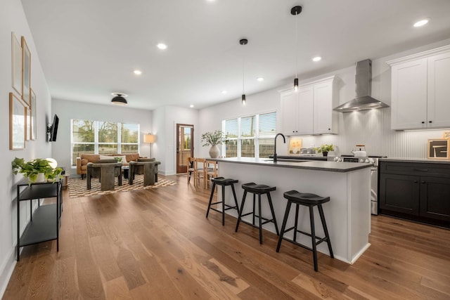 kitchen featuring a kitchen island with sink, stainless steel range with electric cooktop, wood-type flooring, and wall chimney range hood