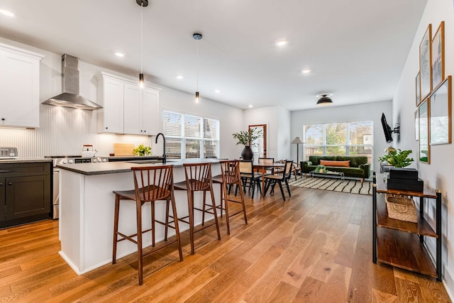 kitchen featuring light hardwood / wood-style floors, white cabinetry, stainless steel range with electric stovetop, and wall chimney range hood