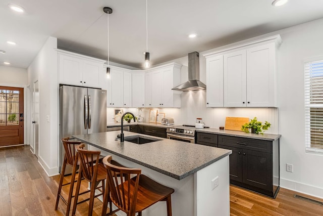 kitchen featuring wall chimney exhaust hood, stainless steel appliances, sink, decorative light fixtures, and light hardwood / wood-style flooring