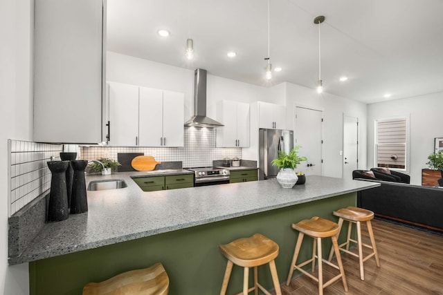 kitchen with a kitchen bar, wall chimney exhaust hood, stainless steel appliances, sink, and white cabinets