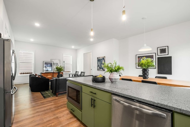 kitchen with appliances with stainless steel finishes, light hardwood / wood-style flooring, hanging light fixtures, and light stone counters