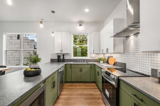 kitchen featuring white cabinets, stainless steel appliances, green cabinets, and wall chimney range hood