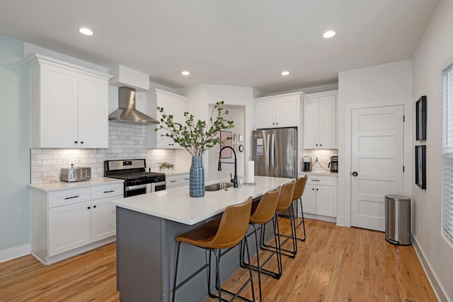 kitchen featuring appliances with stainless steel finishes, sink, wall chimney range hood, white cabinets, and an island with sink