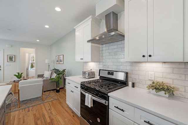 kitchen featuring white cabinets, wall chimney range hood, light hardwood / wood-style flooring, appliances with stainless steel finishes, and tasteful backsplash