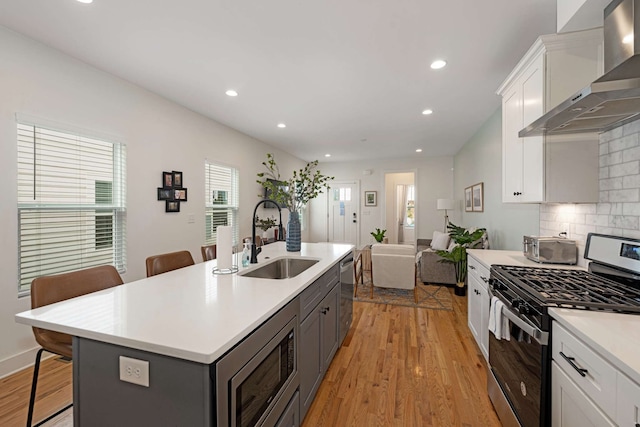 kitchen featuring a kitchen bar, appliances with stainless steel finishes, a kitchen island with sink, wall chimney range hood, and sink