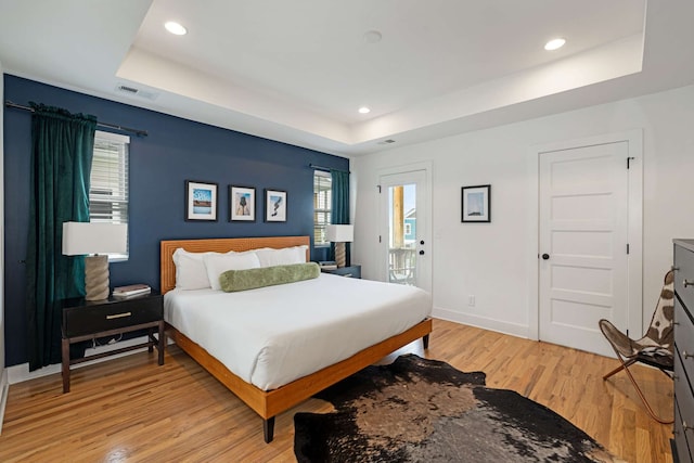 bedroom with light wood-type flooring and a tray ceiling