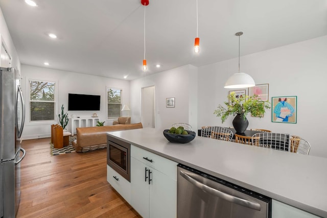 kitchen with hanging light fixtures, light hardwood / wood-style flooring, white cabinets, and stainless steel appliances