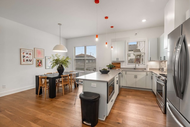 kitchen featuring pendant lighting, hardwood / wood-style floors, white cabinets, sink, and appliances with stainless steel finishes