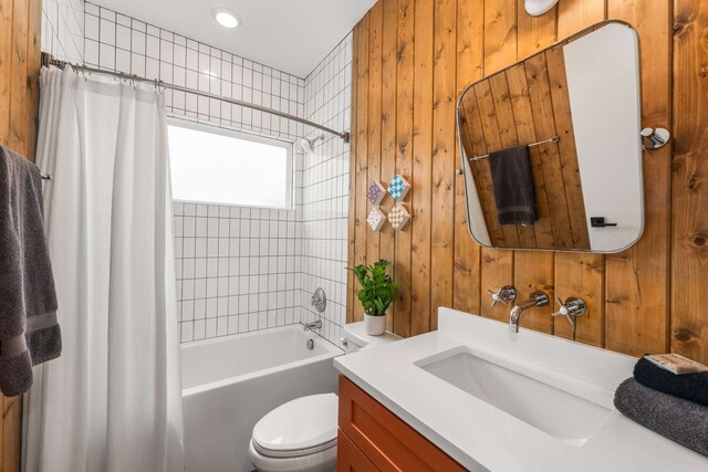 full bathroom with wood walls, shower / bath combo with shower curtain, vanity, and toilet