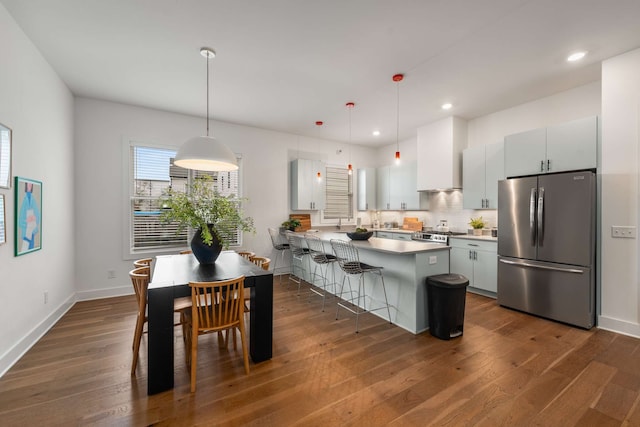 kitchen featuring pendant lighting, a kitchen breakfast bar, stainless steel fridge, dark hardwood / wood-style flooring, and white cabinetry