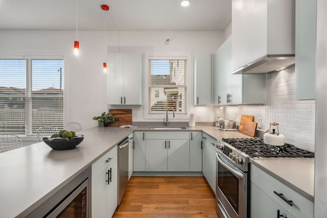 kitchen with appliances with stainless steel finishes, a wealth of natural light, wall chimney exhaust hood, sink, and hanging light fixtures