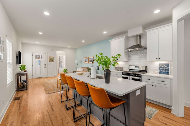 kitchen with a center island with sink, wall chimney exhaust hood, gas stove, and white cabinets