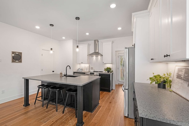 kitchen featuring white cabinetry, sink, wall chimney exhaust hood, an island with sink, and light wood-type flooring