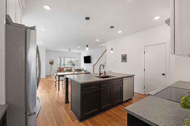 kitchen with sink, pendant lighting, light hardwood / wood-style floors, a kitchen island with sink, and appliances with stainless steel finishes