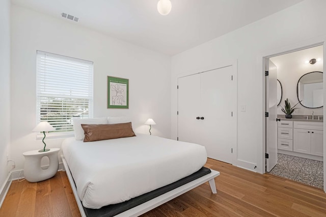 bedroom featuring ensuite bath, a closet, light hardwood / wood-style floors, and sink