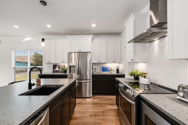 kitchen with wall chimney range hood, sink, light stone countertops, appliances with stainless steel finishes, and decorative light fixtures