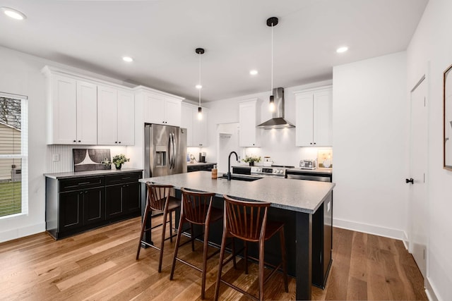 kitchen with a center island with sink, white cabinetry, stainless steel appliances, and wall chimney exhaust hood