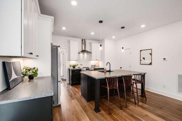 kitchen featuring stainless steel fridge, a kitchen island with sink, wall chimney range hood, light hardwood / wood-style flooring, and white cabinetry