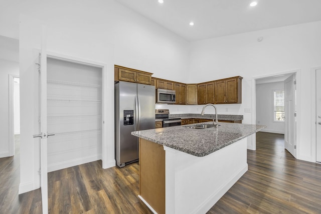 kitchen with dark wood-type flooring, dark stone counters, sink, an island with sink, and appliances with stainless steel finishes