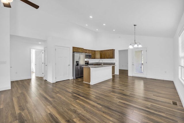 kitchen with stainless steel appliances, hanging light fixtures, dark wood-type flooring, and an island with sink