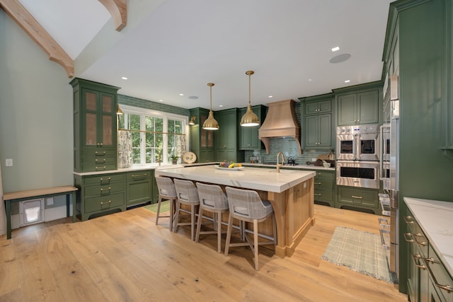 kitchen with green cabinets, a center island with sink, custom exhaust hood, and decorative light fixtures