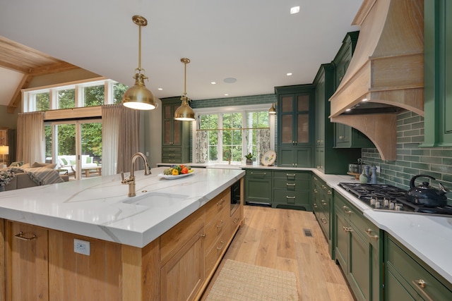 kitchen with light stone counters, a center island with sink, sink, light hardwood / wood-style floors, and stainless steel gas stovetop