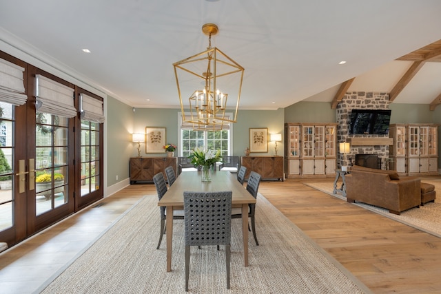 dining area with an inviting chandelier, a fireplace, crown molding, lofted ceiling, and light wood-type flooring